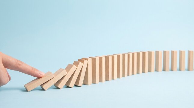Finger pushing first wooden block starting row domino effect on blue background