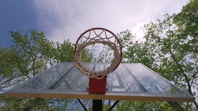 Outdoor Basketball Hoop and Net Low Angle View Against Blue Sky and Trees