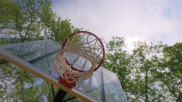 Outdoor Basketball Hoop and Net Low Angle View Against Blue Sky and Trees