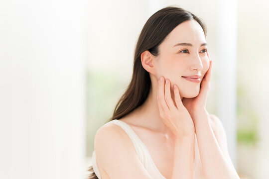 顔を触る笑顔の日本人女性。スキンケアイメージ。