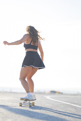 Skater rides on a sunny road with a skateboard wearing a skirt and tank top enjoying the weather © KONSTANTIN SHISHKIN
