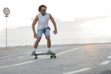 Man rides skateboard along a coastal road as people walk by during sunset © KONSTANTIN SHISHKIN