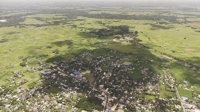 Rural town surrounded by vast green farmland from high altitude drone view, agricultural landscape