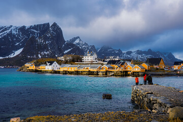 Photographers on a causeway facing a yellow fishing village and turquoise water, Lofoten © dachakrapan