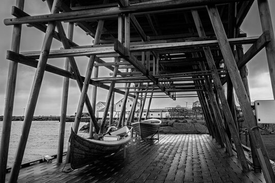 Wooden fishing boats beneath a traditional stockfish drying rack in black and white, Norway