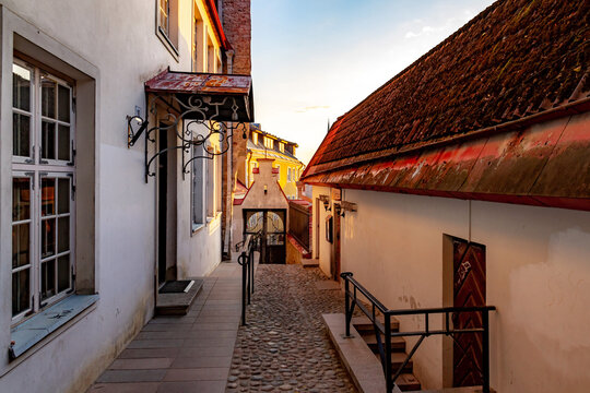 Cozy medieval Lyhike jalg street in the Old Town of Tallinn at dawn. Scenic empty cobblestone alley with historic stone houses, red tile roofs, forged canopy and soft morning light. Estonia.