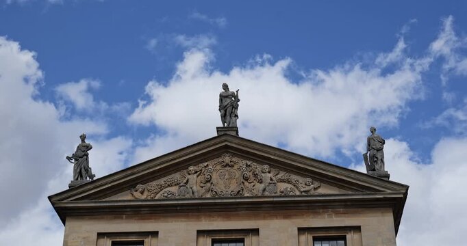 Oxford, Oxfordshire, United Kingdom, August 20, 2026. Statues adorn pediment top on classical university building roof facade.