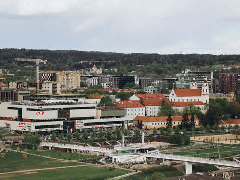 Vilnius, Lithuania - 27 Apr 2025: Panoramic view of Vilnius cityscape with modern buildings, historic church, and green park area under cloudy sky