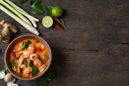 Overhead tom yum goong with fresh herbs on rustic wood