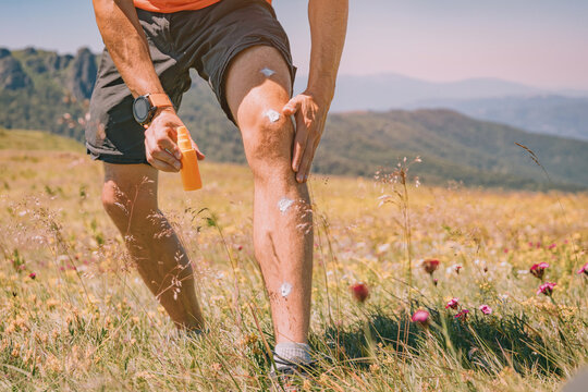Man applying sunscreen lotion on his legs and knees while hiking outdoors in the mountains on a sunny summer day