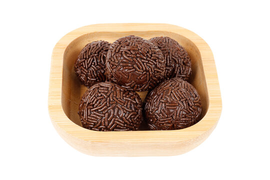 Traditional Brazilian chocolate brigadeiro coated in sprinkles, in a bamboo bowl, isolated on a white background.