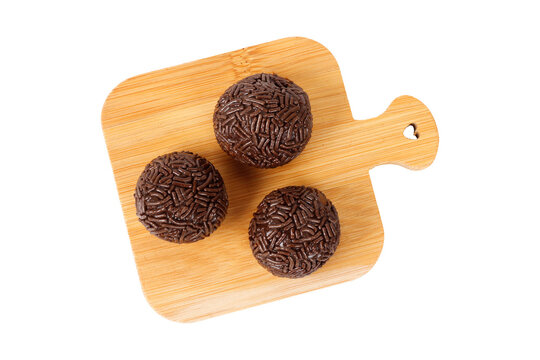 Traditional Brazilian chocolate brigadeiro coated in sprinkles, on a bamboo board, isolated on a white background.