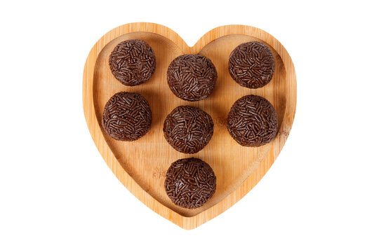 Traditional Brazilian chocolate brigadeiro covered in sprinkles, on a heart shaped bamboo tray, isolated on a white background.