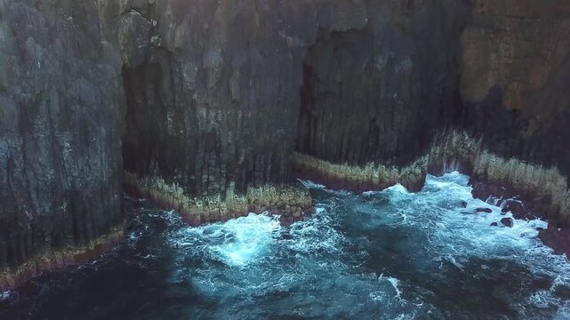 Low drone pass along columnar basalt cliffs battered by Atlantic surf, North Shore Sao Miguel, Azores