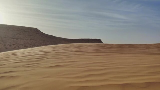 Low-angle look toward a flat-top jebel rising over a curved dune crest in morning light  Sahara scene setter