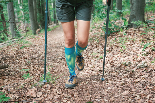 Determined hiker in bright compression socks and trail boots climbs a steep leaf-strewn woodland path with trekking poles. Adventure concept.