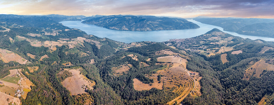 Warm summer light bathes a winding Danube river valley and small riverside town nestled among green forested hills, aerial panorama.