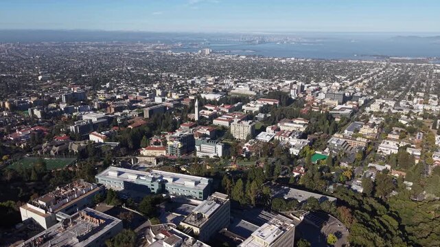 Expansive aerial footage showcasing the University of California, Berkeley campus with the San Francisco Bay and city skyline visible in the distant background under a clear, sunny sky
