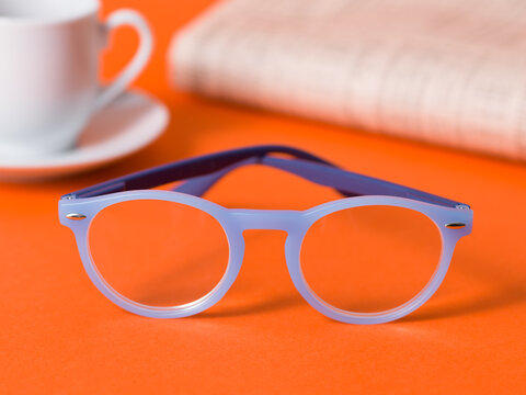 Blue Reading Glasses on Orange Table with Coffee and Newspaper