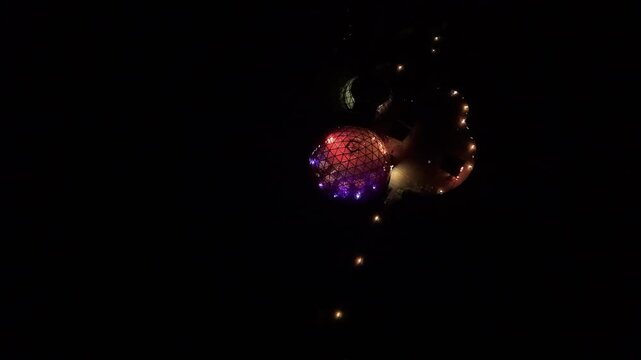 Aerial footage reveals a glowing geodesic dome with vivid purple and red lights, surrounded by illuminated string lights in deep darkness, creating a striking night composition.