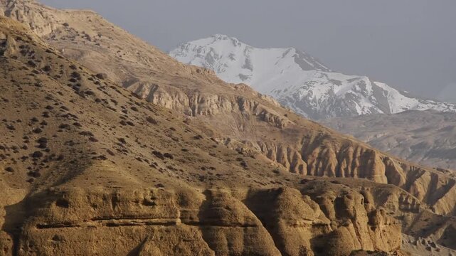 Slow pan across eroded canyon badlands at sunset with a snow-capped Annapurna-range peak beyond, Upper Mustang, Nepal