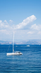 Fototapeta premium Monohull sailing yacht anchored in clear blue sea near the coast of Corfu island in Greece during a partly cloudy day, summer vacation concept