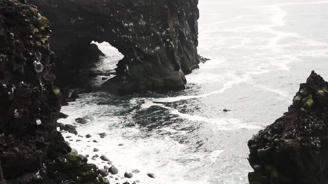 Static shot of sea arch and cliffs at Londrangar with waves surging below nesting seabirds, Snaefellsnes Peninsula