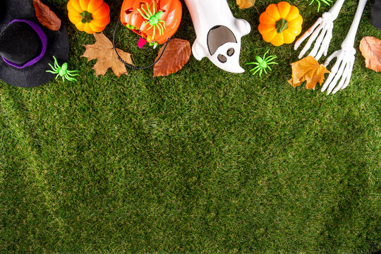 Trick or treat Halloween holiday outdoor party background. Various Halloween accessories, ghost decoration, basket with candies, colorful pumpkins, autumn fall leaves on green grass lawn background