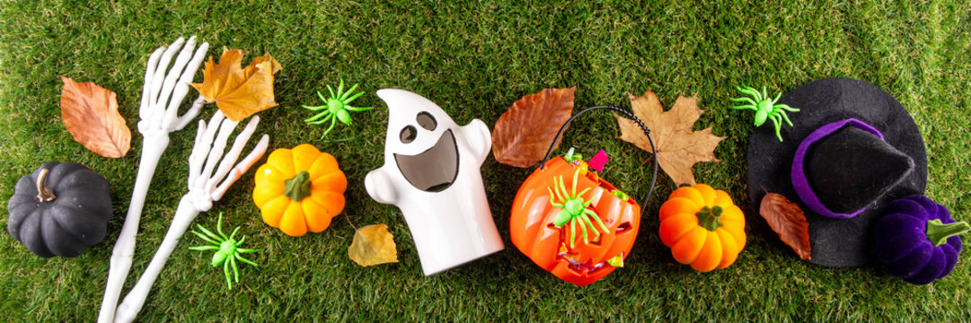 Trick or treat Halloween holiday outdoor party background. Various Halloween accessories, ghost decoration, basket with candies, colorful pumpkins, autumn fall leaves on green grass lawn background
