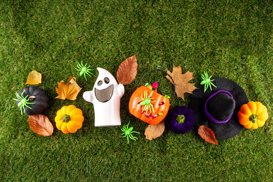 Trick or treat Halloween holiday outdoor party background. Various Halloween accessories, ghost decoration, basket with candies, colorful pumpkins, autumn fall leaves on green grass lawn background