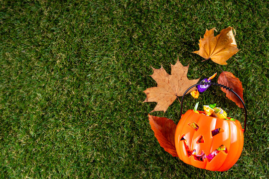 Trick or treat Halloween holiday outdoor party background. Various Halloween accessories, ghost decoration, basket with candies, colorful pumpkins, autumn fall leaves on green grass lawn background