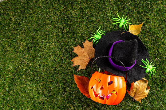 Trick or treat Halloween holiday outdoor party background. Various Halloween accessories, ghost decoration, basket with candies, colorful pumpkins, autumn fall leaves on green grass lawn background