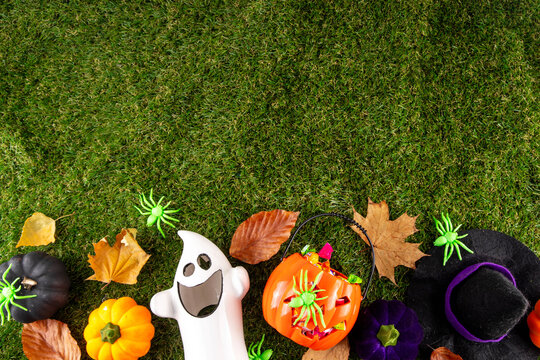 Trick or treat Halloween holiday outdoor party background. Various Halloween accessories, ghost decoration, basket with candies, colorful pumpkins, autumn fall leaves on green grass lawn background