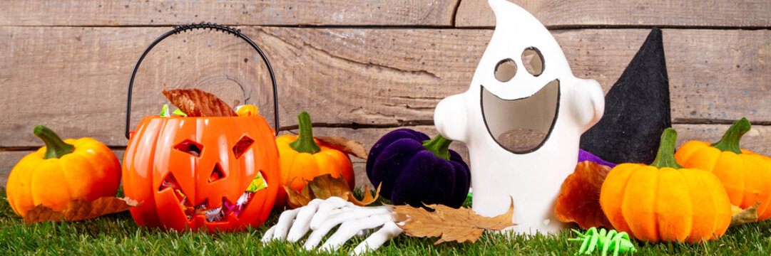 Trick or treat Halloween holiday outdoor party background. Various Halloween accessories, ghost decoration, basket with candies, colorful pumpkins, autumn fall leaves on green grass lawn background
