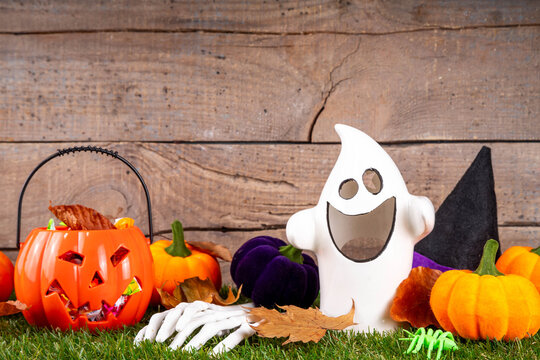 Trick or treat Halloween holiday outdoor party background. Various Halloween accessories, ghost decoration, basket with candies, colorful pumpkins, autumn fall leaves on green grass lawn background