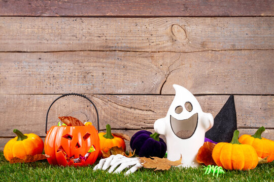 Trick or treat Halloween holiday outdoor party background. Various Halloween accessories, ghost decoration, basket with candies, colorful pumpkins, autumn fall leaves on green grass lawn background