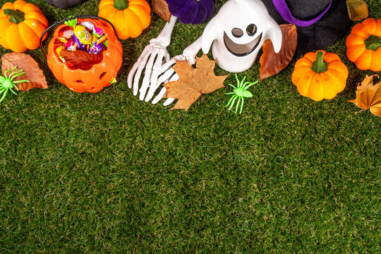 Trick or treat Halloween holiday outdoor party background. Various Halloween accessories, ghost decoration, basket with candies, colorful pumpkins, autumn fall leaves on green grass lawn background