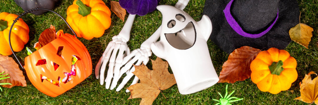 Trick or treat Halloween holiday outdoor party background. Various Halloween accessories, ghost decoration, basket with candies, colorful pumpkins, autumn fall leaves on green grass lawn background