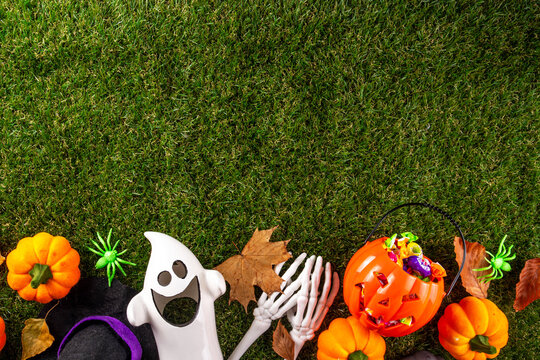 Trick or treat Halloween holiday outdoor party background. Various Halloween accessories, ghost decoration, basket with candies, colorful pumpkins, autumn fall leaves on green grass lawn background