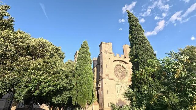 pan over Fortified west front and rose window of Cathedrale Saint-Nazaire framed by cypresses, Beziers, Herault, France