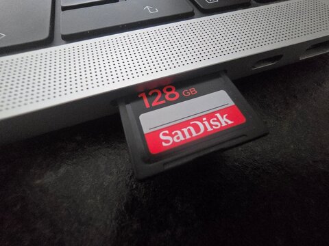 Close-up of a 128GB SanDisk SDXC memory card inserted into the side card reader slot of a laptop, highlighting portable flash storage technology, data storage capacity, and digital file transfer hardw