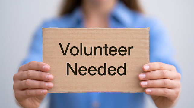 Person holding cardboard sign with volunteer needed text message recruitment help support community service program charity work non profit organization