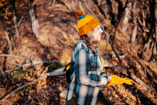 Happy woman in autumn forest enjoying active outdoor walk - seasonal outdoor activity. Smiling female hiker wearing bright yellow accessories. Wellness and connecting with nature trend.