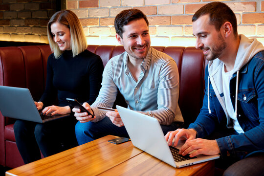Diverse young adult Caucasian colleagues working on laptops and making online payment with credit card in cafe. Image suitable for e-commerce, digital banking, and remote work marketing
