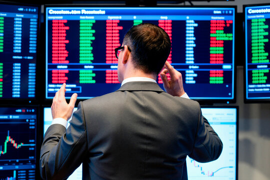 Rear view of Caucasian young adult male stock trader analyzing financial data on multiple screens. Image represents market analysis and is suitable for fintech advertising