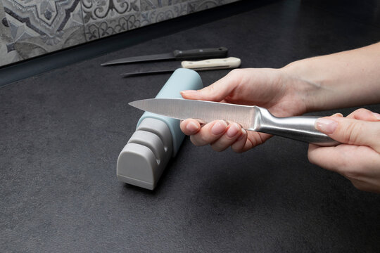 Person inspecting a sharpened stainless steel kitchen knife after completing the blade sharpening process. Concept of knife inspection, sharpness, kitchen maintenance, cooking equipment, home care.