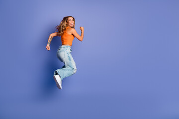 Fototapeta premium Young woman jumping in orange singlet against purple background showcasing fashion fitness and joy