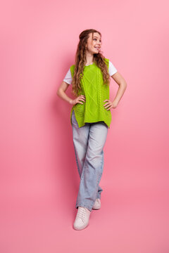 Joyful young female model wearing bright green knit vest posing against pink background for fashion and lifestyle shot