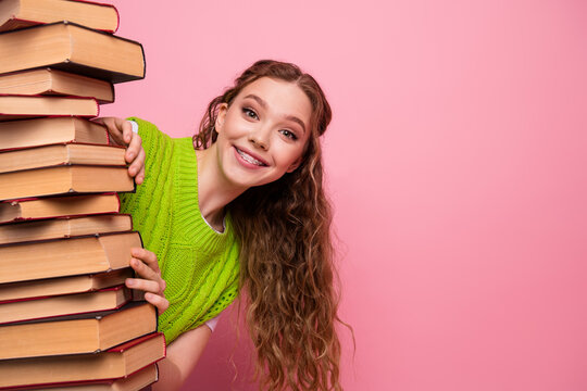 Young woman with a stack of book smiles brightly while wearing a green sweater in a pink studio creating a cheerful studious lifestyle
