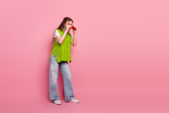 Young woman with bright green vest posing playfully against pink background showcasing casual fashion and cheerful vibe